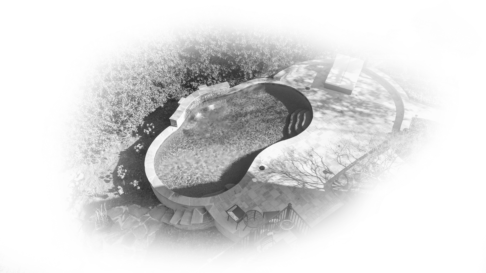 Aerial view of a kidney-shaped backyard pool with patio chairs, surrounded by trees and landscaping, with a soft, white vignette effect around the edges.