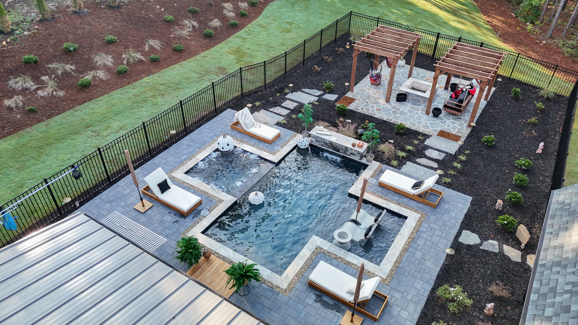 Aerial view of a backyard swimming pool with lounge chairs on the patio and two wooden pergolas in the corner.